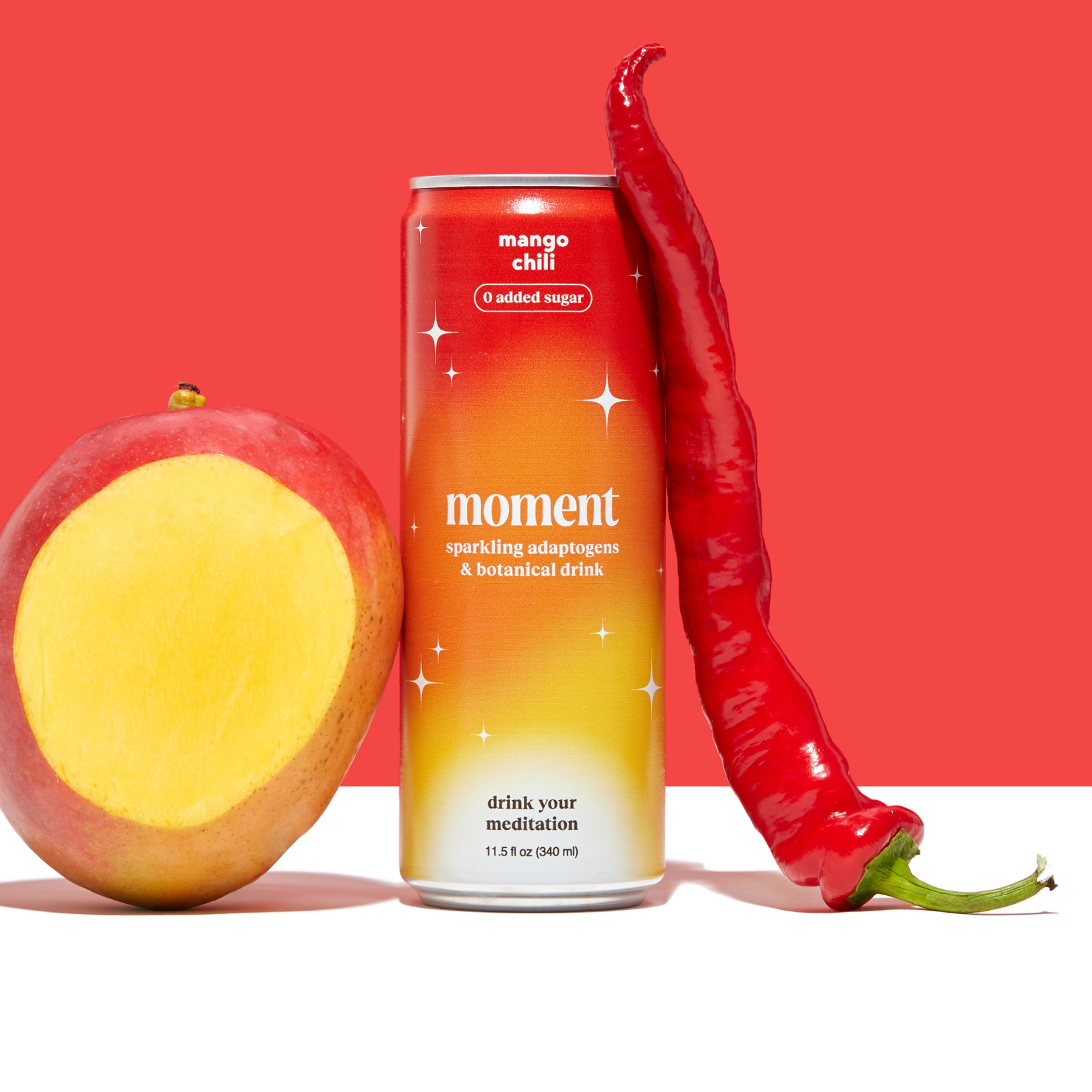 Can of Moment mango chili sparkling drink with a mango slice and chili pepper against a red background.