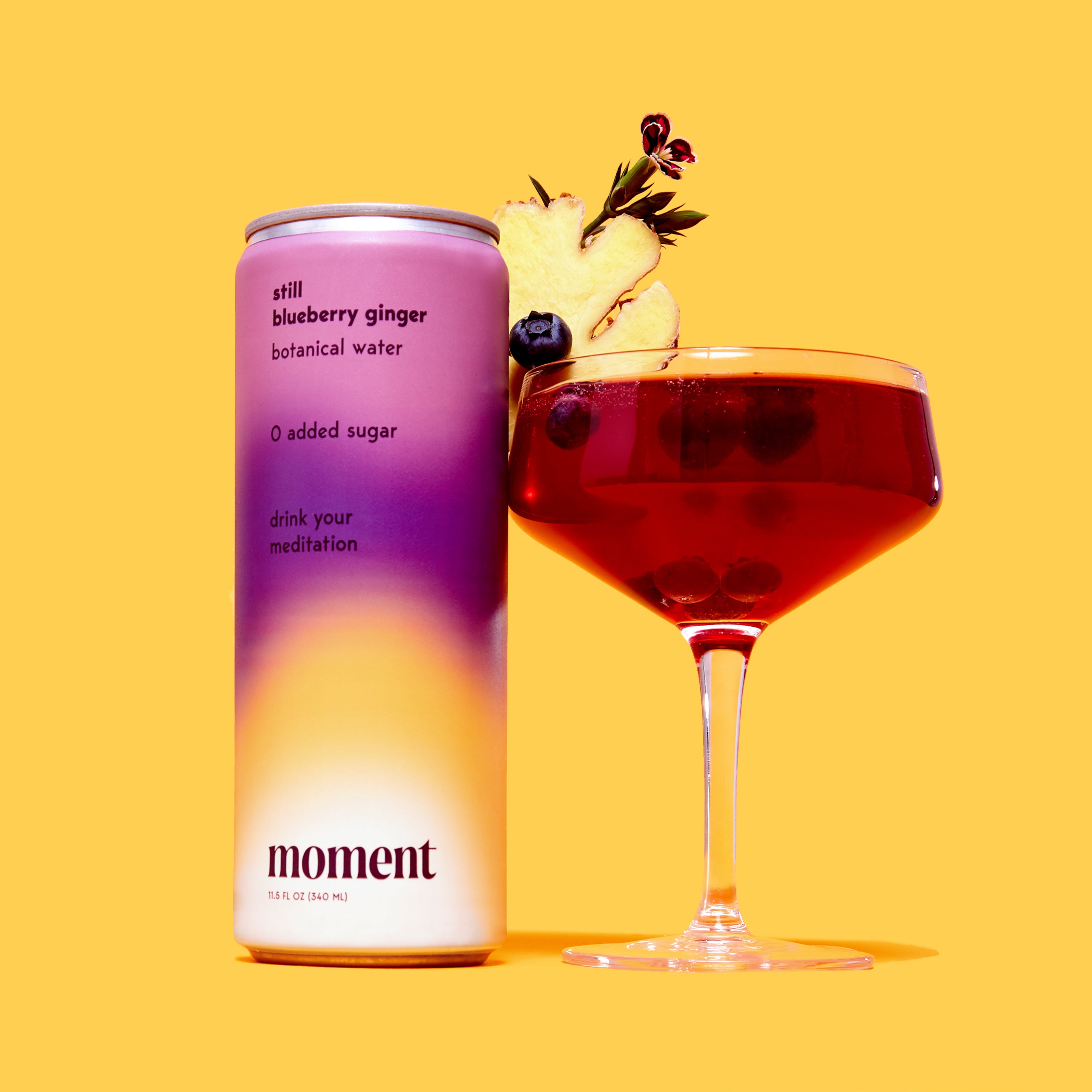 A can of 'moment' blueberry ginger water next to a cocktail glass, against a yellow background.
