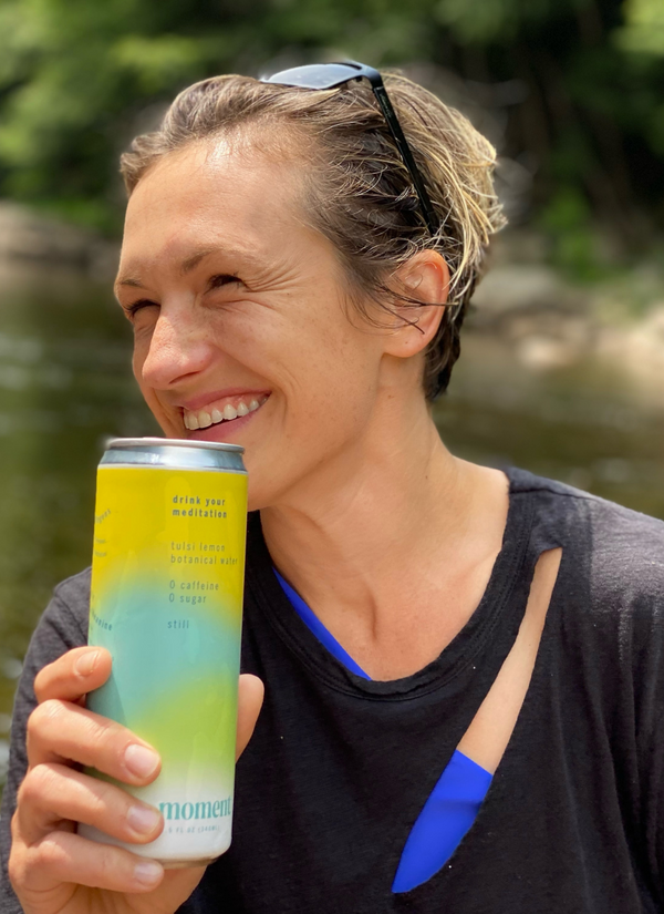 Woman smiling and holding a can of drink outdoors.