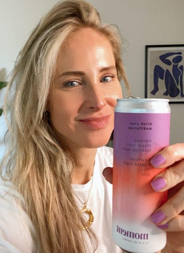 Woman smiling at camera, holding a pink beverage can, with minimal background detail.