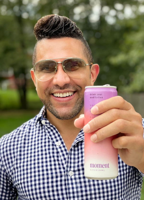 Smiling man holding a pink can with the text 'moment' outdoors.
